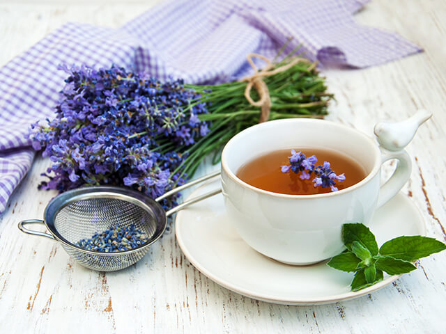 A glass cup of herbal chamomile tea with fresh flowers on a wooden surface